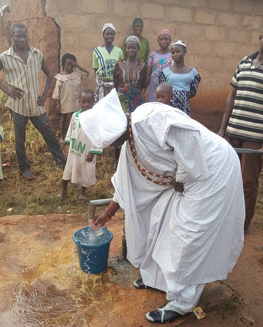 Fadare about to drink the water while the villagers admire.